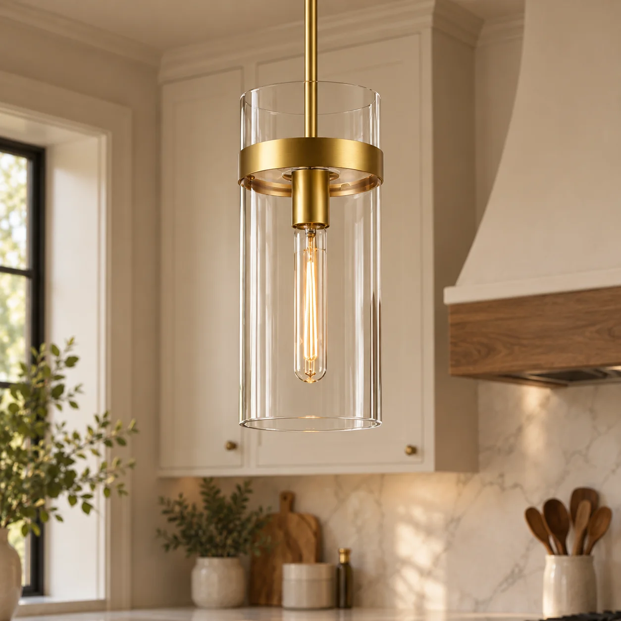 Clear cylindrical glass pendant light with brushed brass trim and an exposed filament bulb
