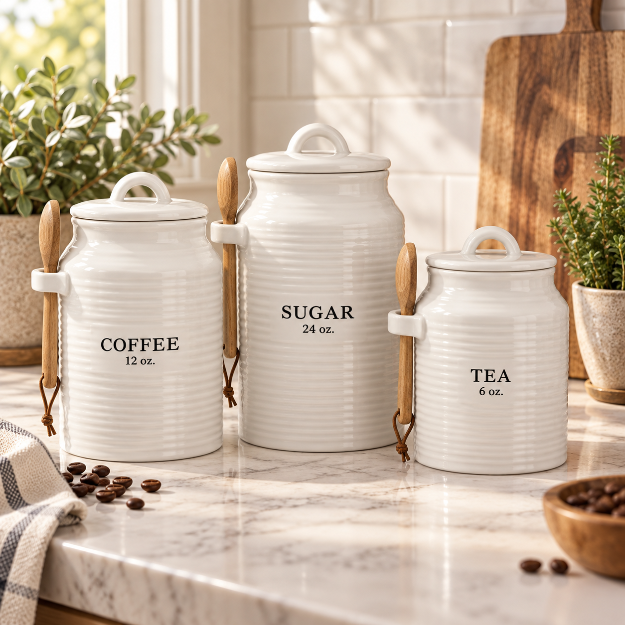 Three white ribbed ceramic canisters labeled coffee, sugar, and tea with wooden spoons in side holders on a marble counter.