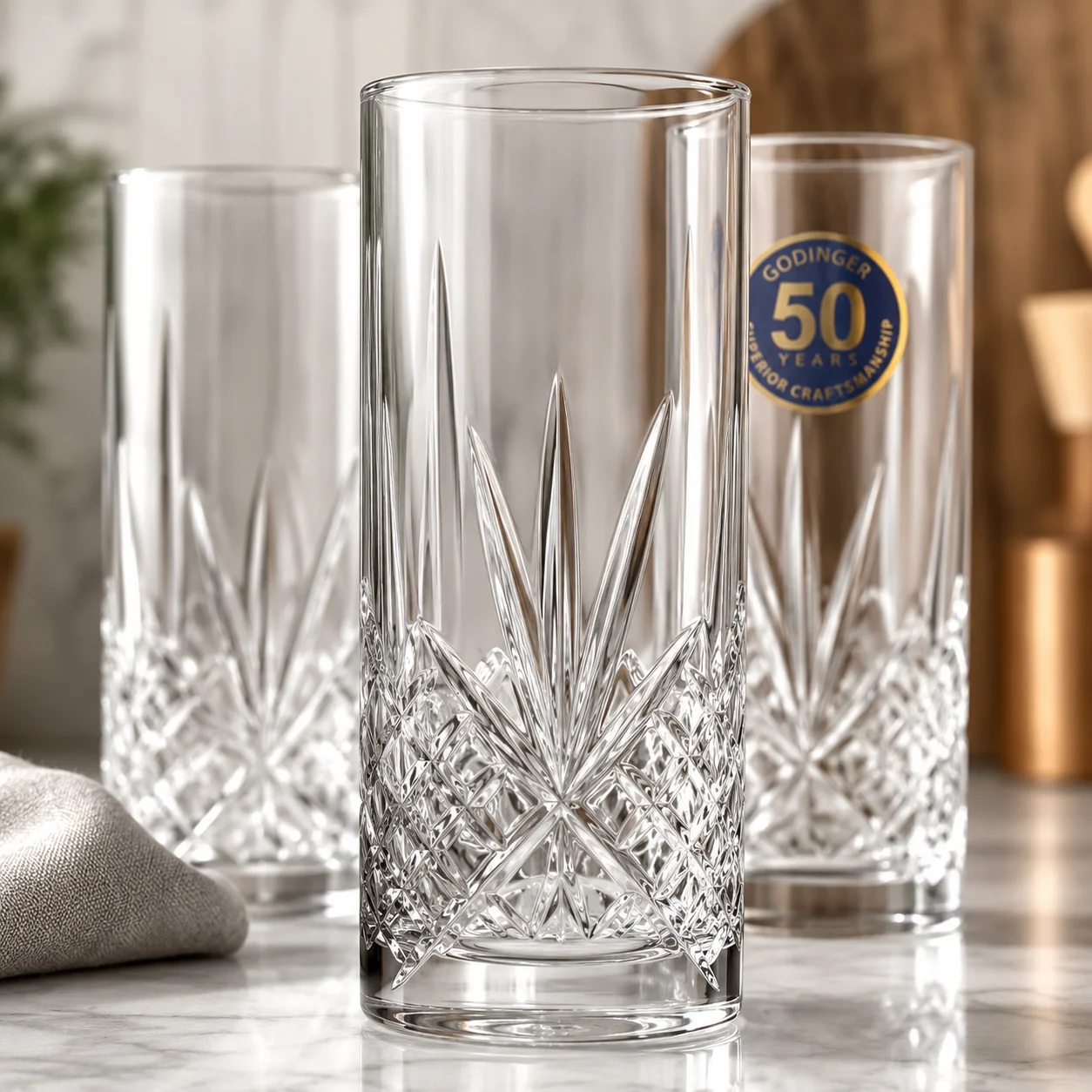 Three tall cut-glass highball tumblers on a marble countertop