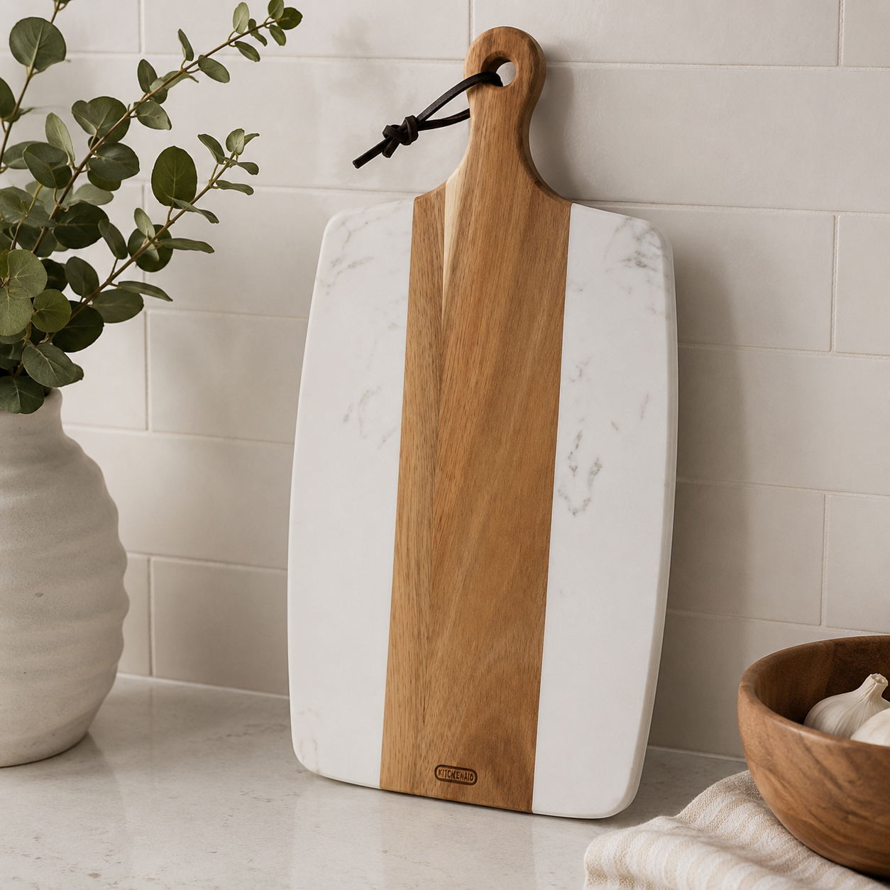 Paddle board with white marble sides and a central wood stripe leaning against a tiled wall next to a vase and wooden bowl.