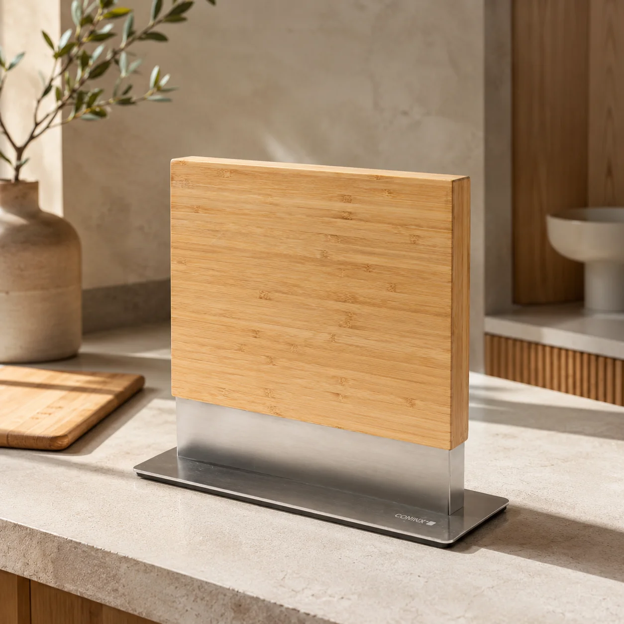 Light wood magnetic knife block standing upright on a stainless steel base on a stone countertop
