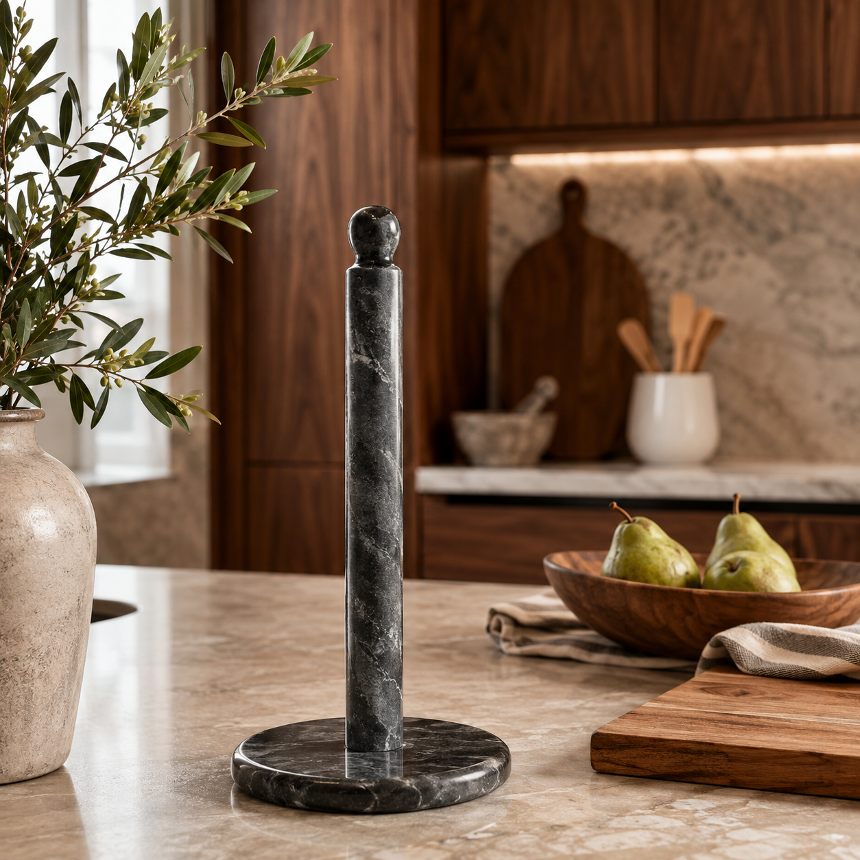 Black marble paper towel holder with round stone base styled on a warm neutral kitchen countertop.